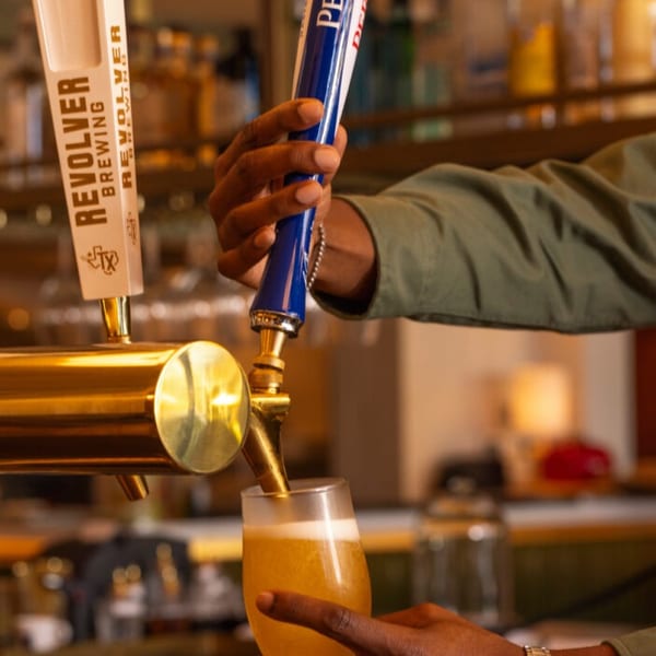 Bartender pouring a golden beer from a Peroni tap into a glass at a bar.